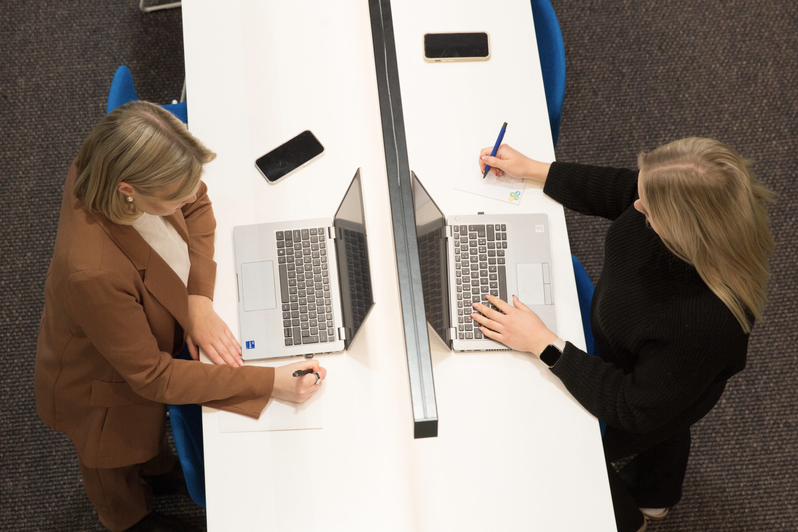Kaksi naista tekemässä töitä tietokoneiden ääressä.
