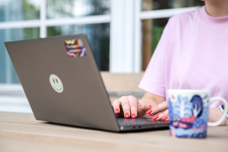 Nainen on tietokoneella ja juo kahvia.